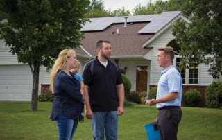 Young couple, members of Dakota Electric, stand outside their home after just installing rooftop solar panels.