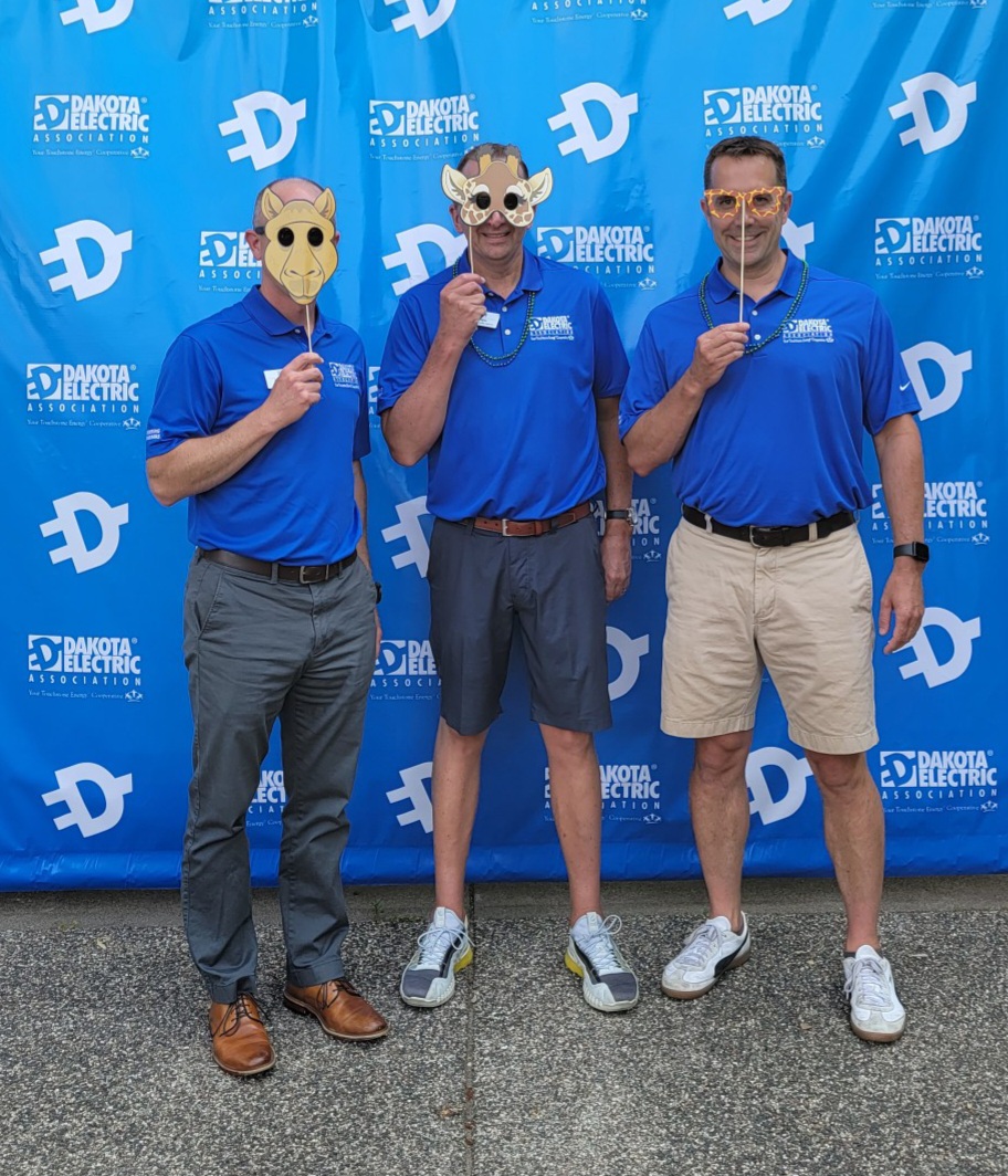 Three Dakota Electric staff members standing in front of a photo wall wearing silly masks.